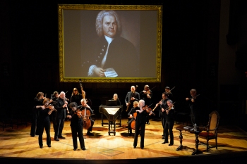 Tafelmusik Baroque Orchestra performing The Circle of Creation with a portrait of Bach on a screen.